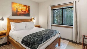 Ein Schlafzimmer mit einem hölzernen Bett, einem Nachttisch, einer Lampe, einem Bild von einem Reh und einem Fenster mit Vorhängen.