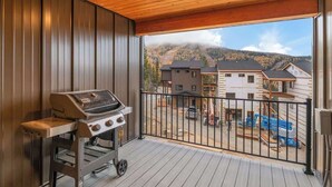 Ein Balkon mit Grill, Holzboden und Blick auf Häuser und Berge.