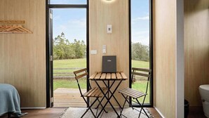 Une pièce avec une table et des chaises en bois, un ordinateur portable posé sur la table et une vue sur un espace verdoyant par une grande fenêtre.