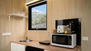 Une cuisine compacte équipée d’un four à micro-ondes, d’un grille-pain et d’une machine à café sur le plan de travail, d’une fenêtre au-dessus de l’évier et d’une étagère où sont rangés des verres.
