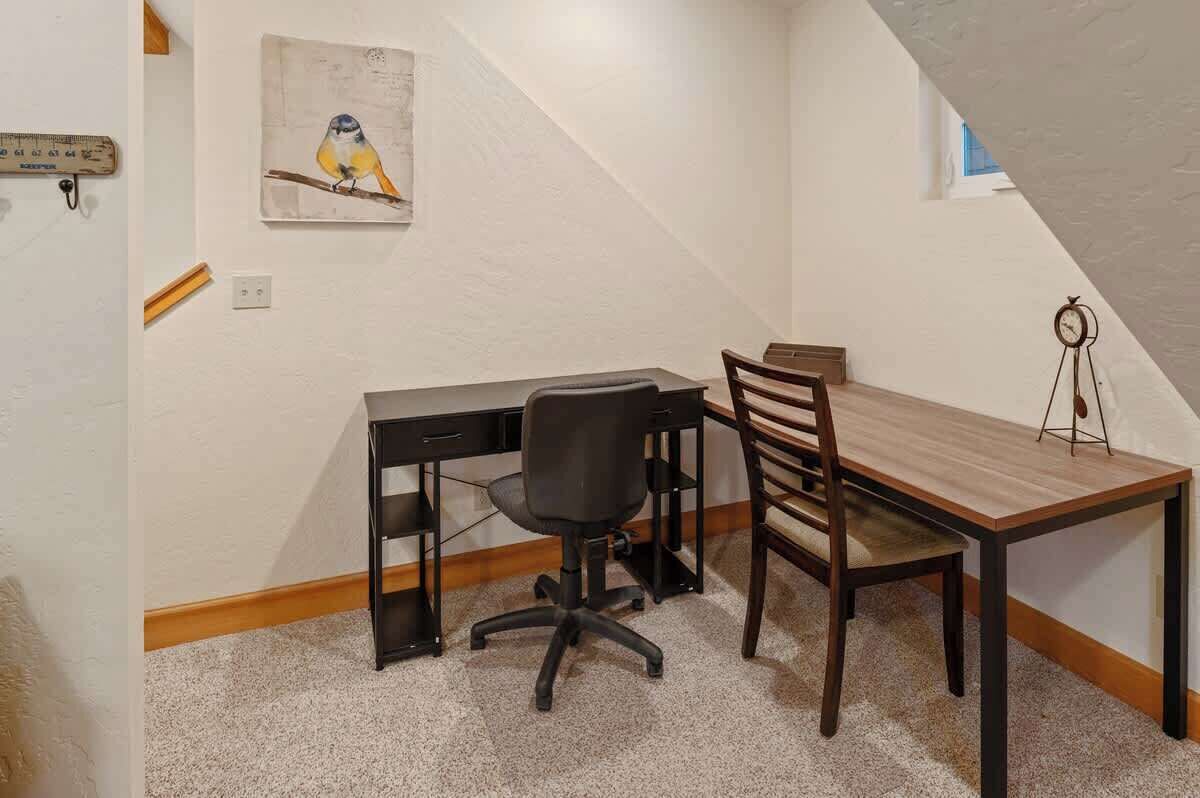A small room with a desk, chair, and a dining table. There is a painting on the wall and a clock on the wall.