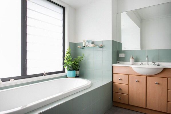 A modern bathroom with a freestanding bathtub, a large mirror, and a vanity with a sink. - Stunning spacious home 5 minutes walk to beach, full kitchen, games room (Bawley Point)