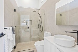 A modern bathroom with a glass-enclosed shower, a white sink, and a toilet.
