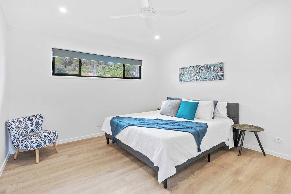 A bedroom with a bed, a chair, a window, and a ceiling fan.