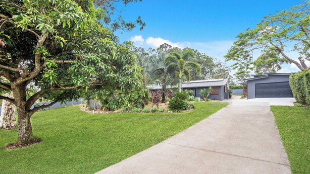 A residential driveway leading to a garage, surrounded by well-maintained grass and various trees. - Escape to Alawara (Tallai)