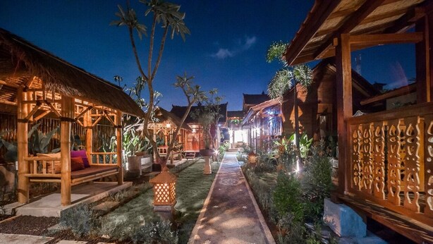 A well-lit pathway leading to a traditional wooden structure with a thatched roof, surrounded by lush greenery and decorative lanterns. - The Lebak Canggu (Canggu)