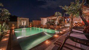 A nighttime pool area with a rectangular pool, lounge chairs, and a wooden deck. - The Lebak Canggu (Canggu)