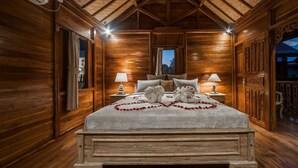 A wooden cabin-style bedroom with a large bed, two bedside lamps, and a nightstand. - The Lebak Canggu (Canggu)