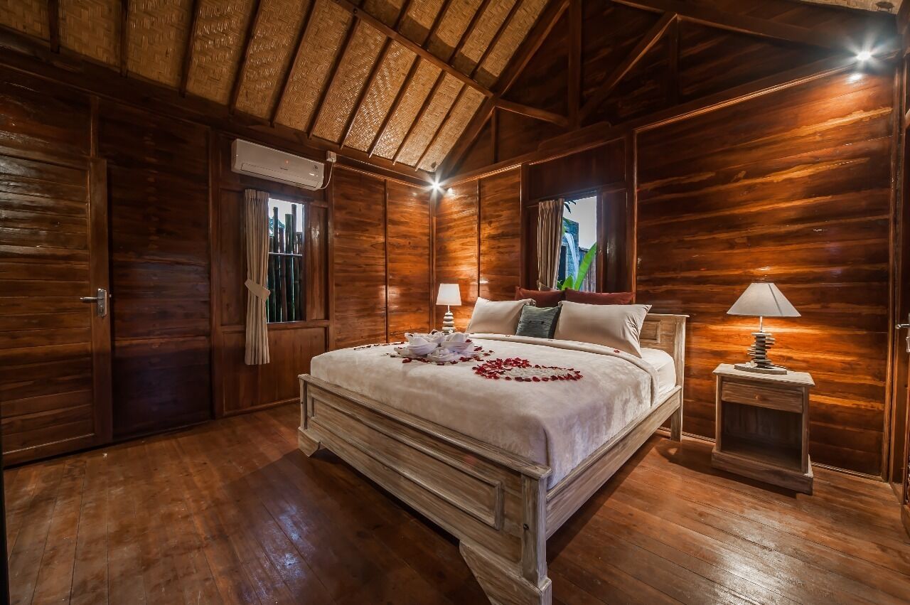 A wooden-paneled bedroom with a bed, two bedside lamps, and a window with curtains.