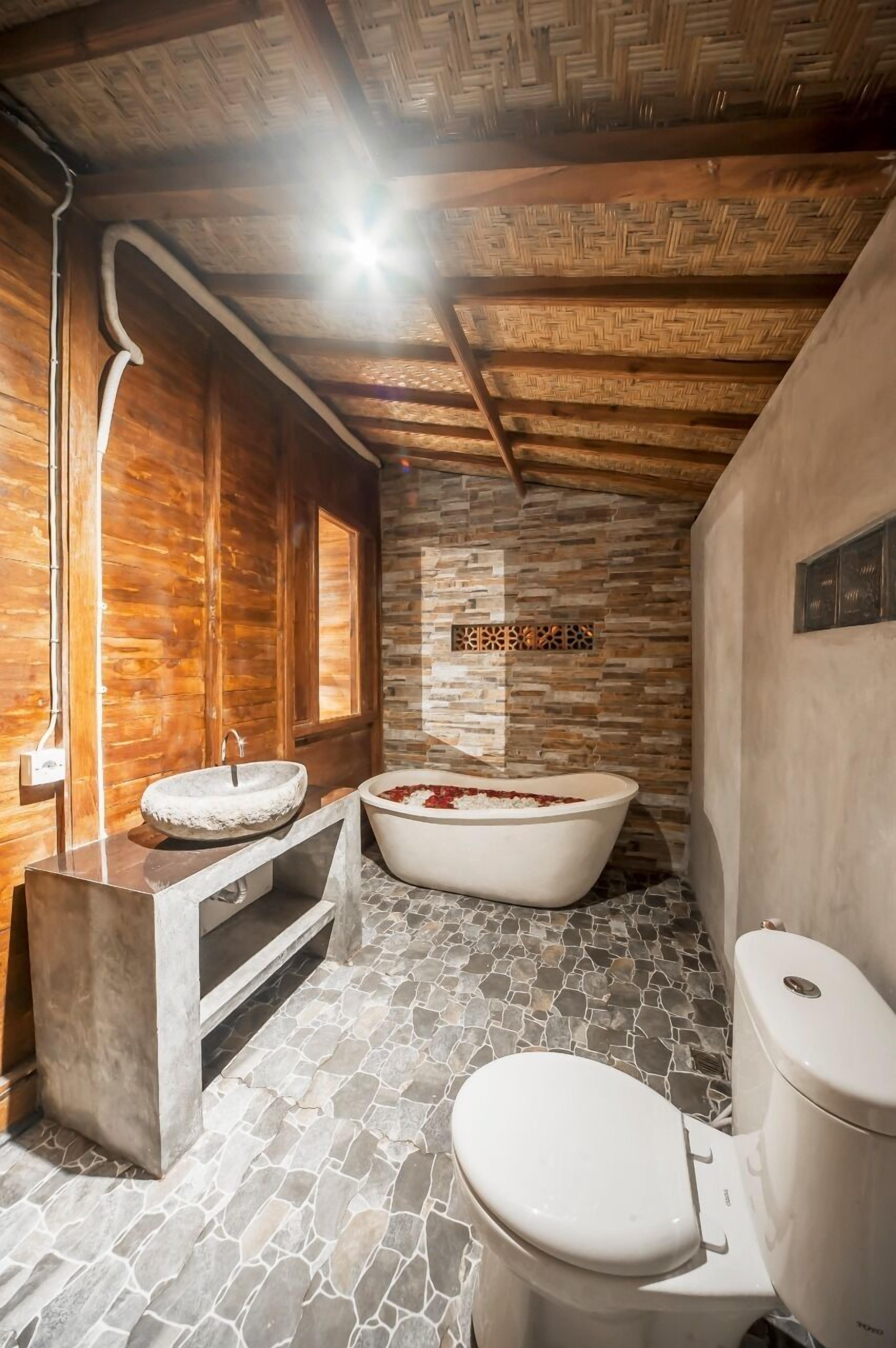 A bathroom with a stone floor, a freestanding bathtub, a sink, and a toilet.