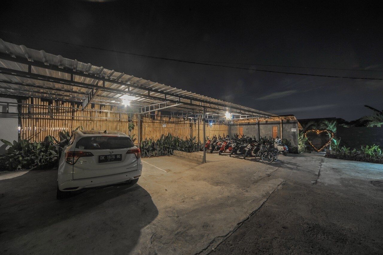 A covered outdoor area with a car parked in front, a row of motorcycles, and a heart-shaped light decoration.
