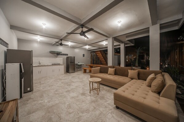 A spacious living area with a large beige sofa, a small round table, and a kitchen in the background. - The Lebak Canggu (Canggu)