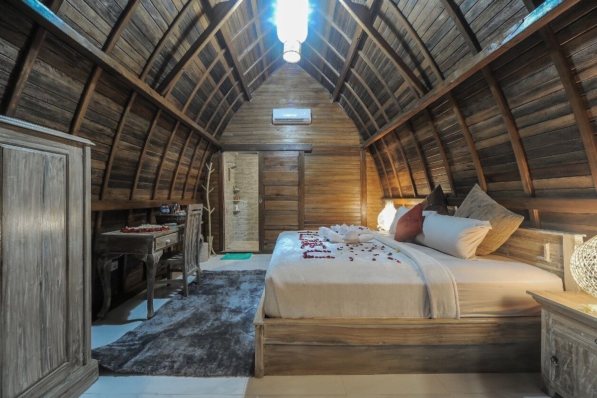Une chambre confortable située sous les toits, avec un plafond en bois incliné, un lit avec des oreillers, une table de chevet et une commode.