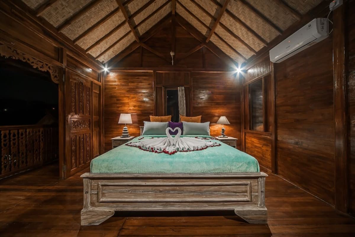 Une pièce en bois avec un lit, deux tables de chevet, un ventilateur de plafond et une fenêtre.