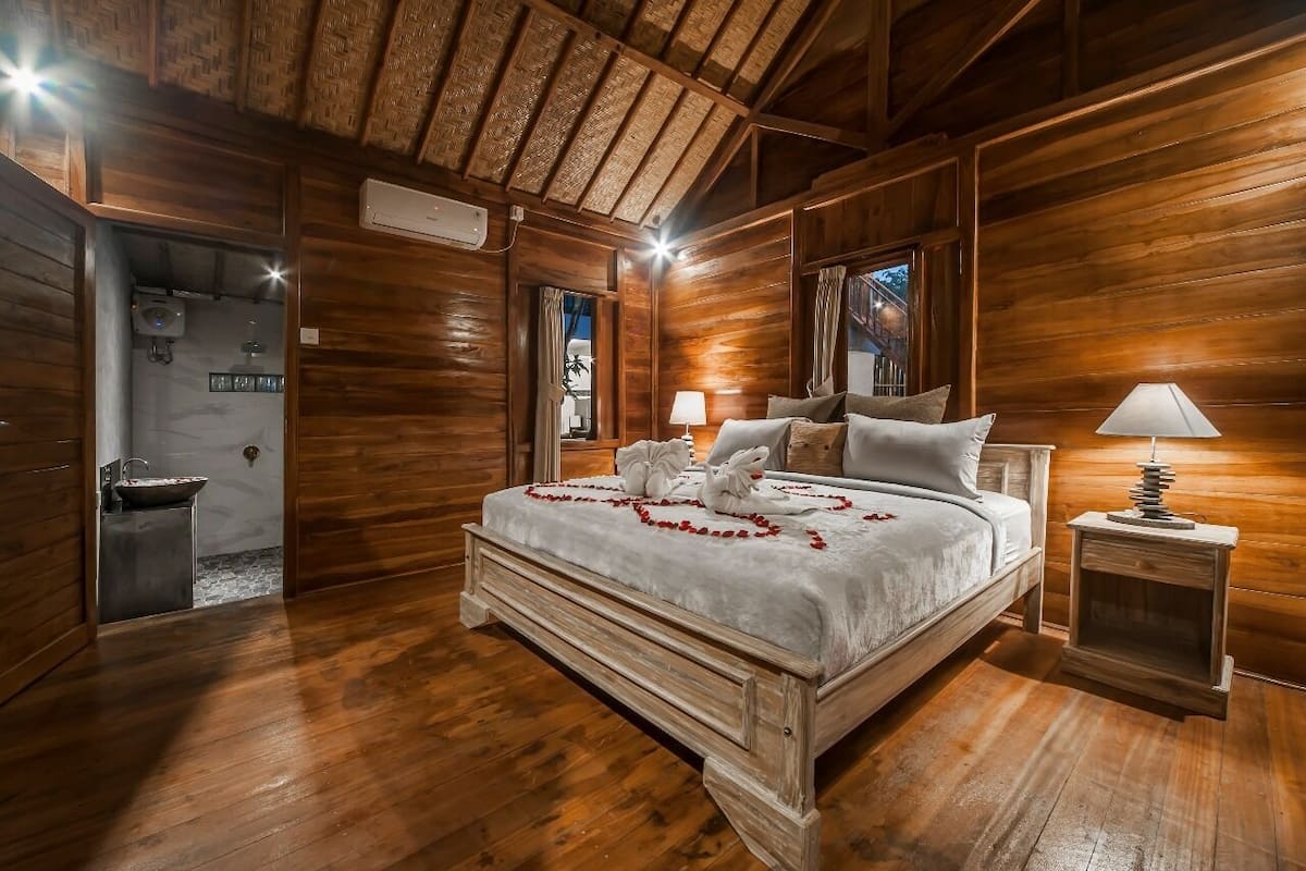 Une chambre à coucher aux murs lambrissés, avec un lit, des lampes de chevet et une vue sur l’extérieur.