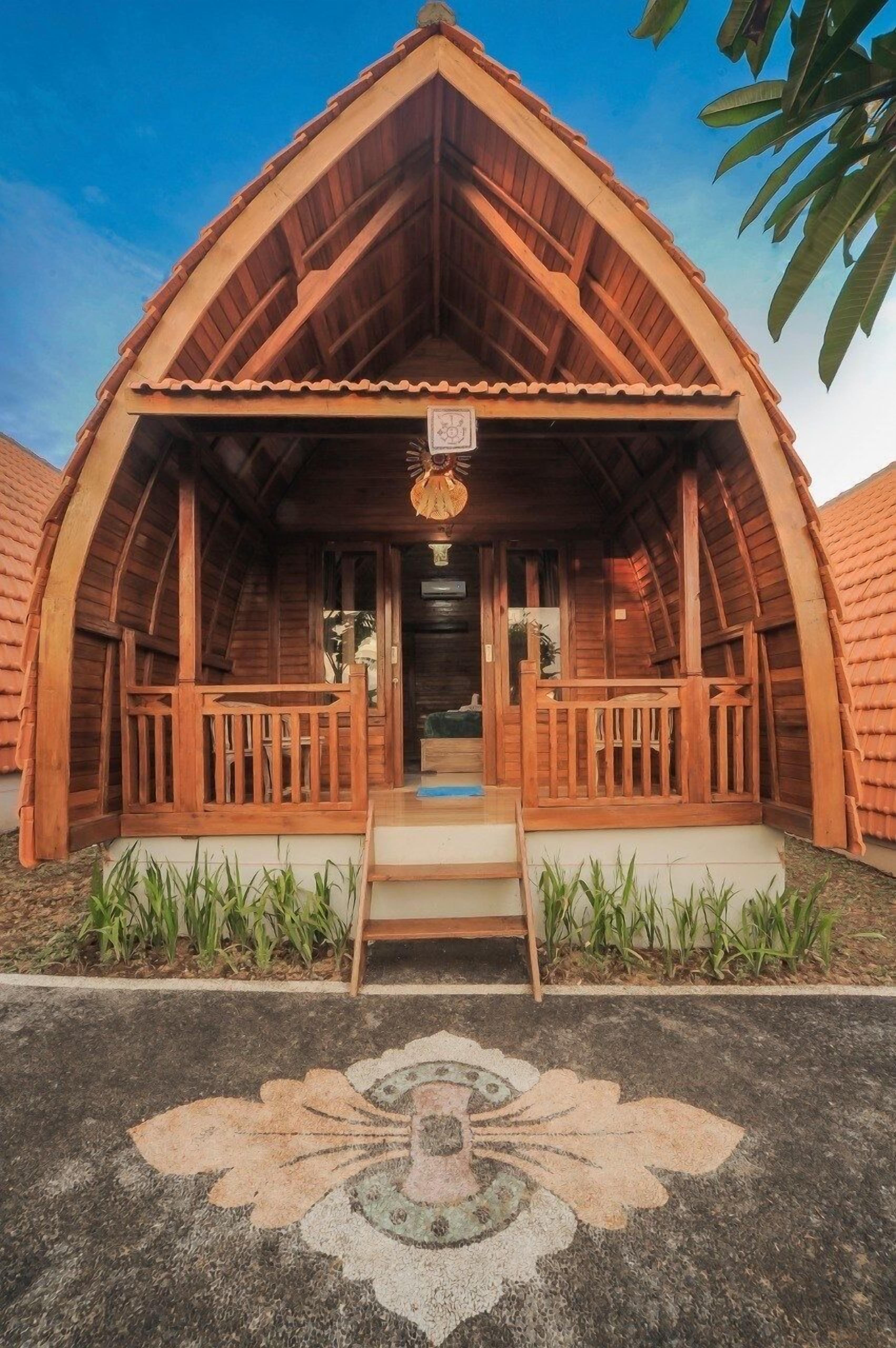 A wooden cabin with a pitched roof, a porch with railings, and a small staircase leading to the entrance.