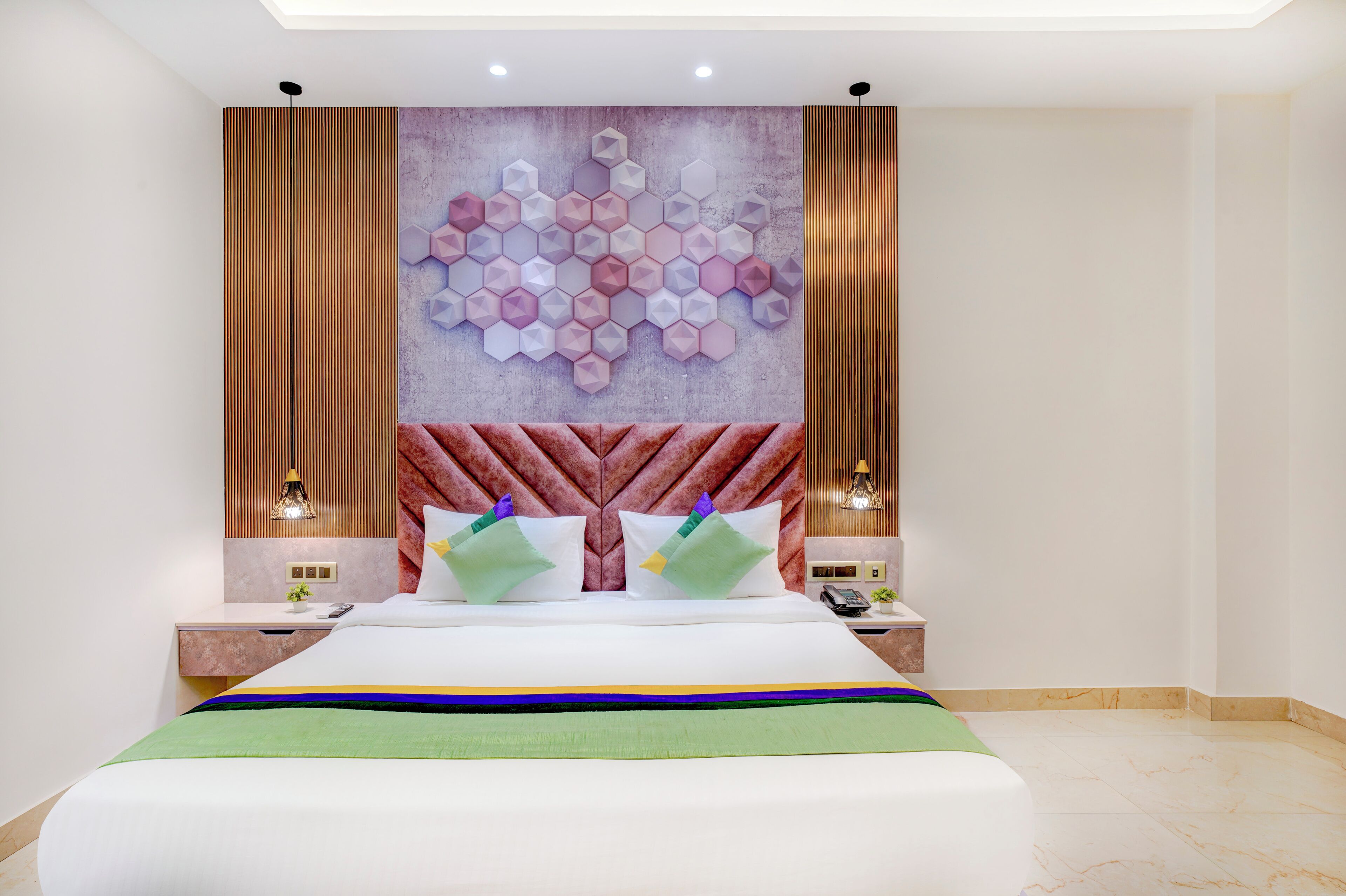 A modern hotel room with a large bed, a decorative wall, and two bedside tables with lamps.