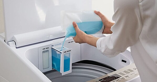 A person pouring blue liquid into a washing machine.