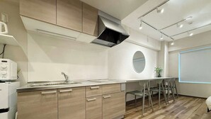 A modern kitchen with wooden cabinets, a stainless steel sink, and a built-in stove. There is a round mirror on the wall and a dining area with chairs. - Fully Equipped Studio Getaway (Hiroshima)