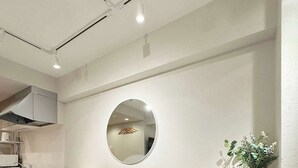 A modern kitchen with a long countertop, four chairs, a round mirror, and a potted plant. - Fully Equipped Studio Getaway (Hiroshima)