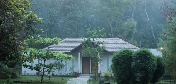 A single-story building with a tiled roof, surrounded by lush greenery and trees. - Abad Brookside (Vythiri)