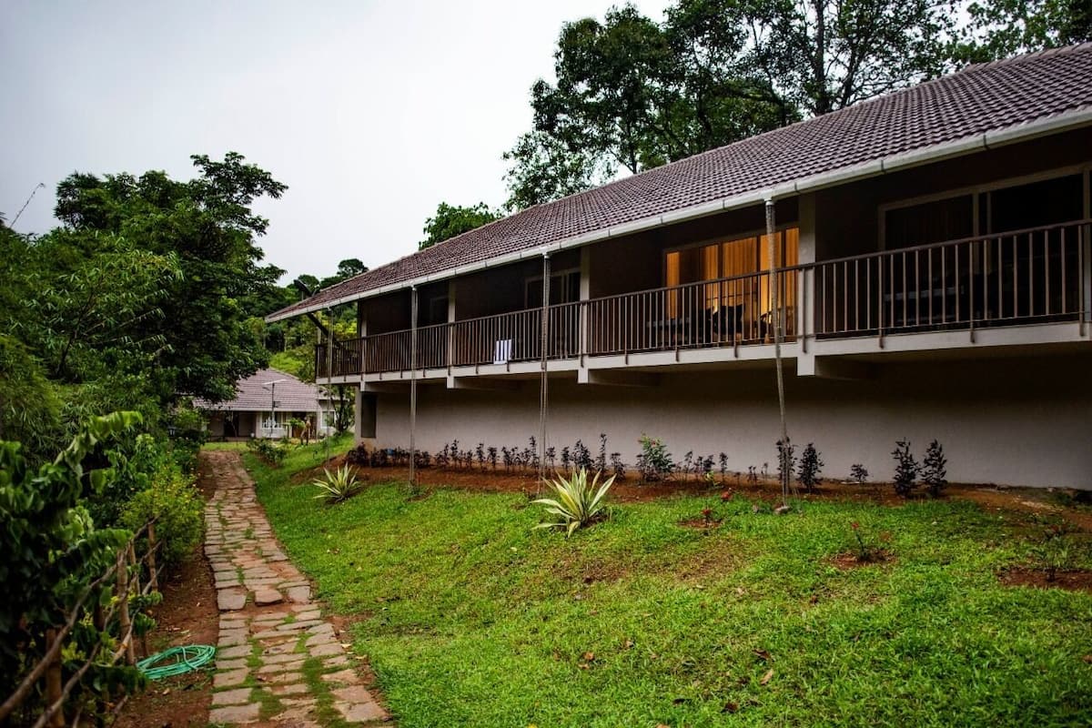 A two-story building with a tiled roof, a balcony on the upper floor, and a paved pathway leading to a small structure in the background.