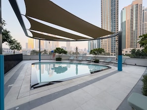 A rooftop swimming pool with lounge chairs and a view of tall buildings.