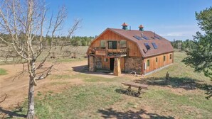 A rustic barn with a wooden exterior, a stone foundation, and a large open porch. - Rustic Barn on 51 Acres (Cripple Creek)