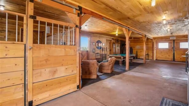 A spacious indoor area with wooden walls and a concrete floor, featuring a pool table and seating area. - Rustic Barn on 51 Acres (Cripple Creek)