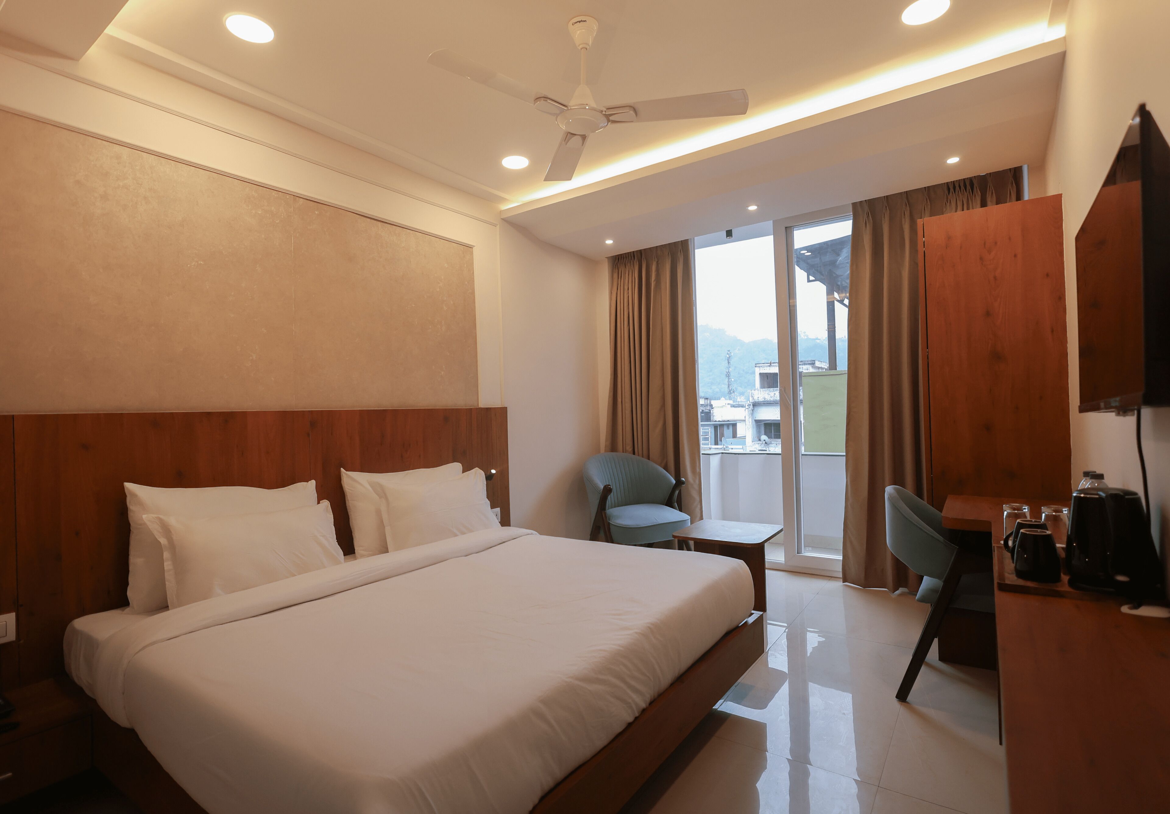 A hotel room with a large bed, a desk, a chair, and a ceiling fan.