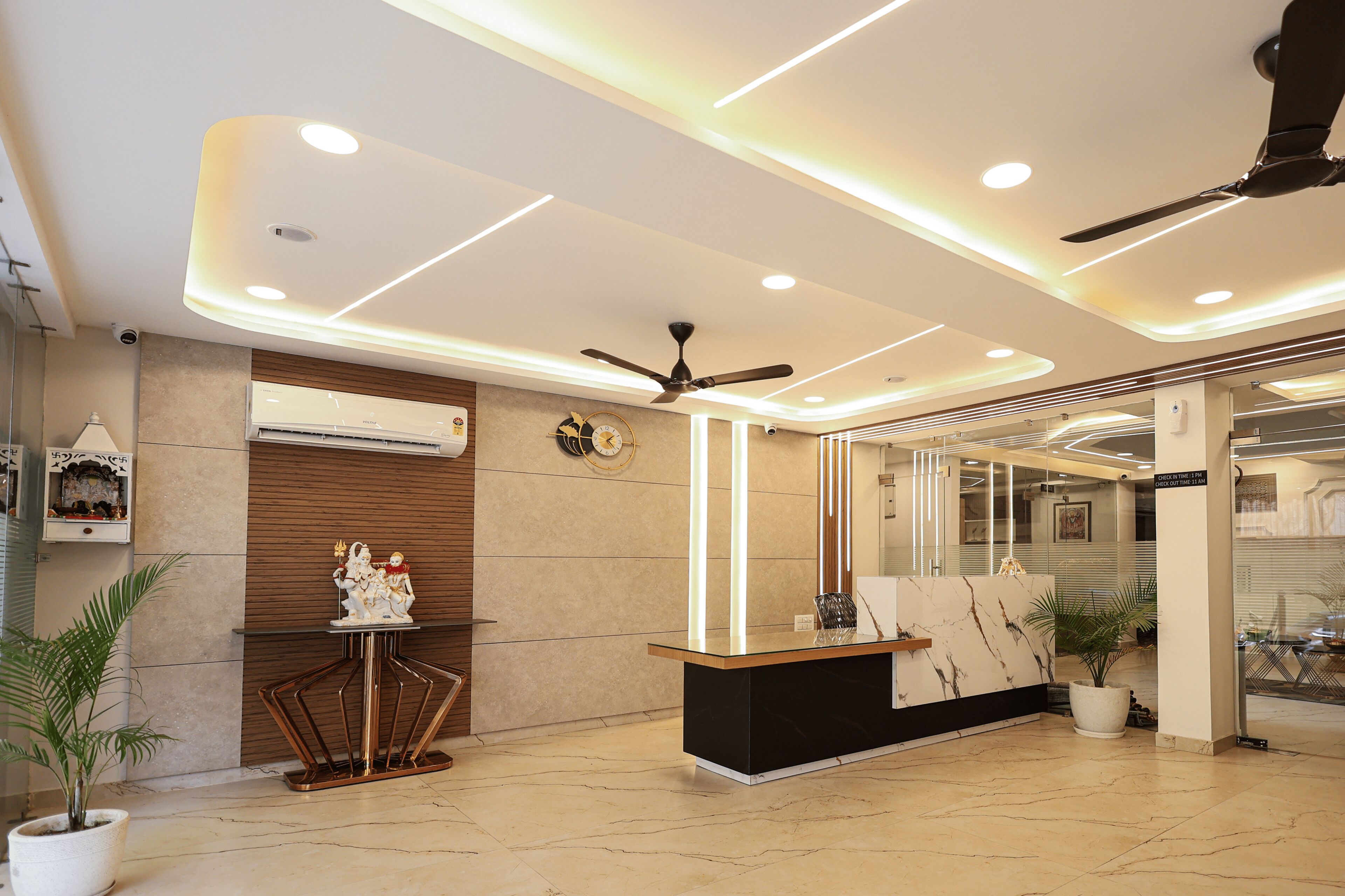 A modern reception area with a marble floor, a reception desk, ceiling fans, recessed lighting, and potted plants.