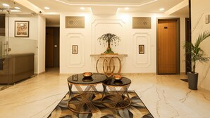 A lobby with a marble floor, two black tables with gold frames, a central decorative tree, and a wooden door labeled "007". - Arjun - A boutique hotel (Haridwar)