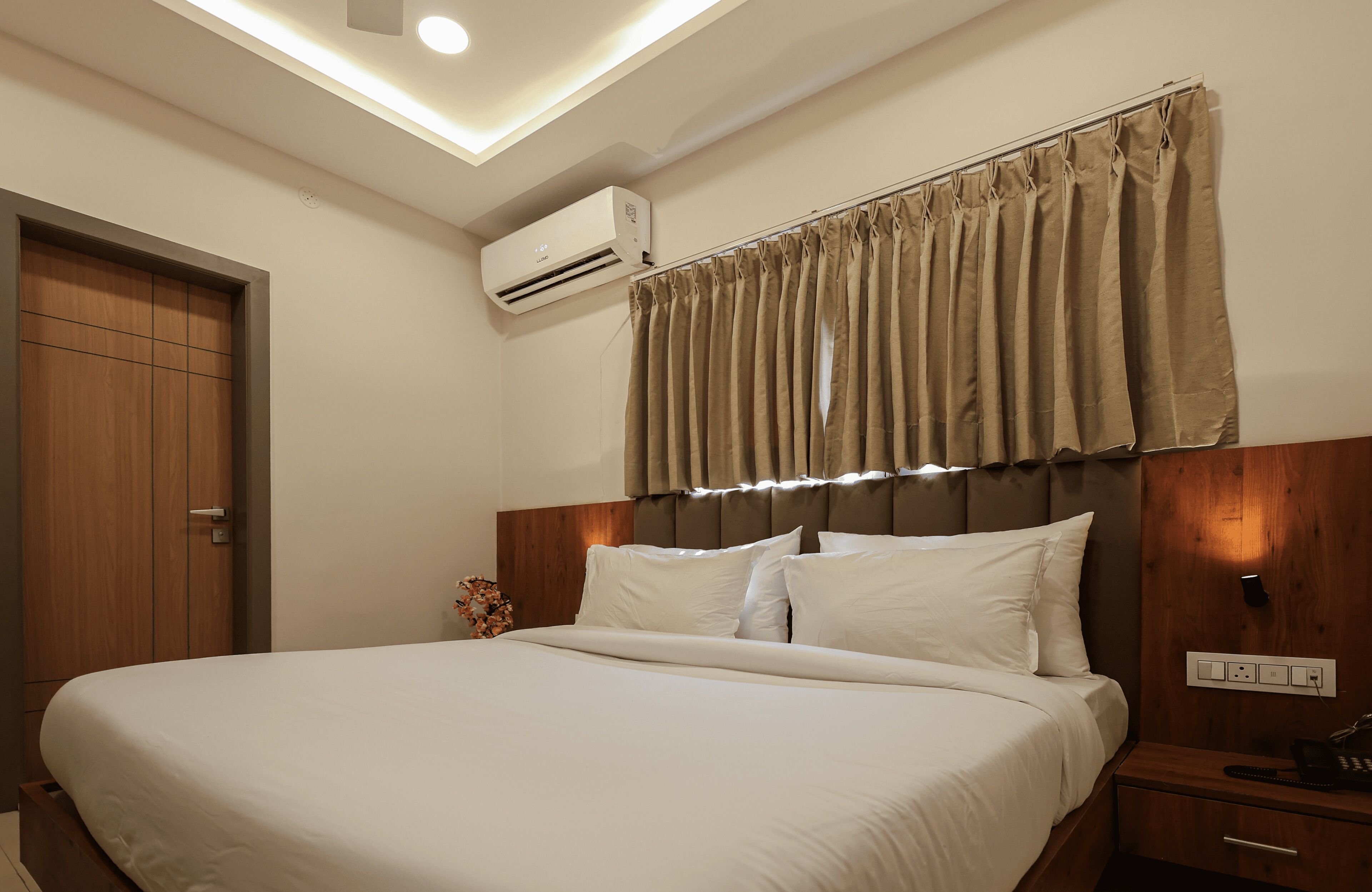 A neatly made bed with white linens, a wooden headboard, and a beige curtain above.