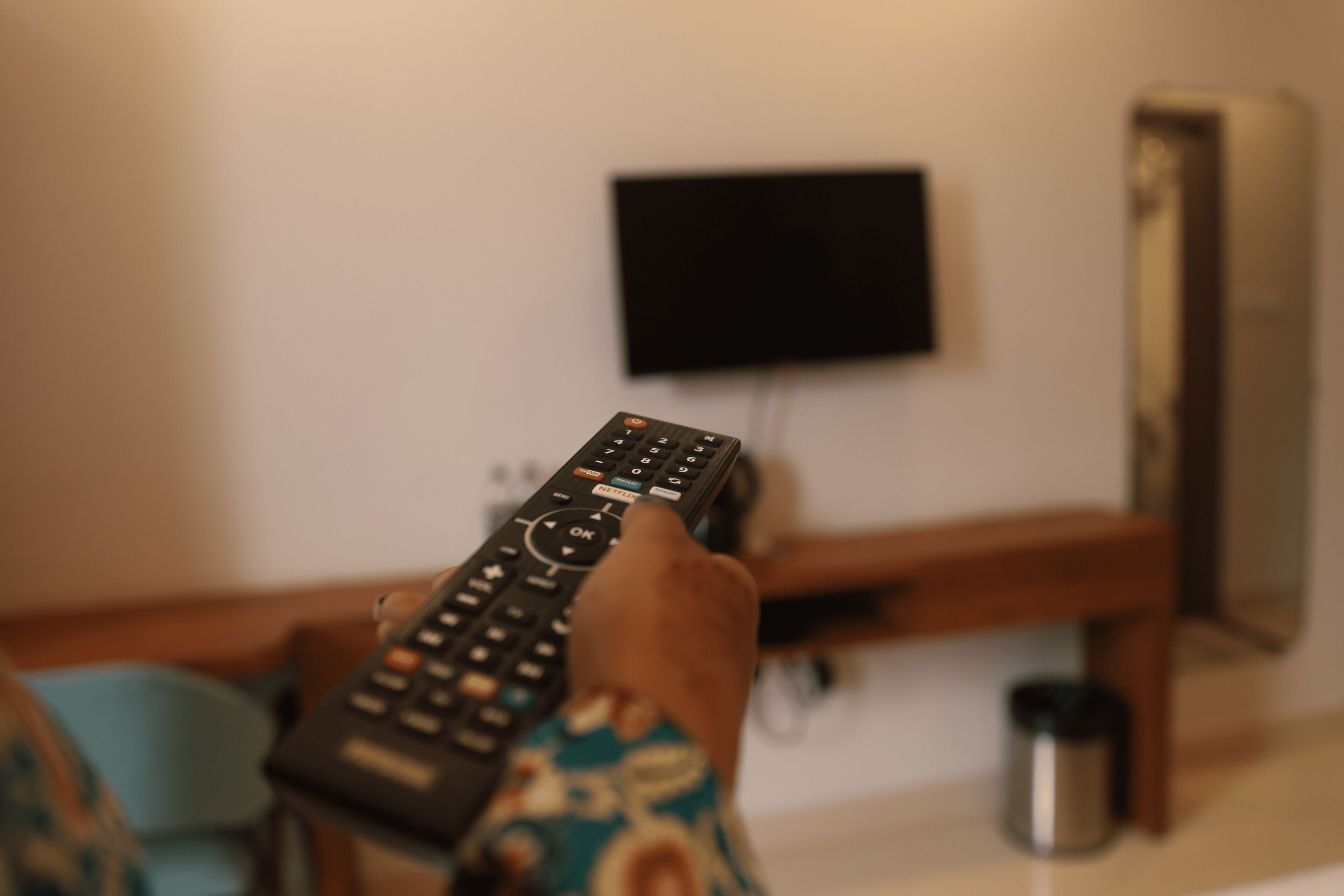 Una mano sostiene un control remoto frente a un televisor instalado en la pared.