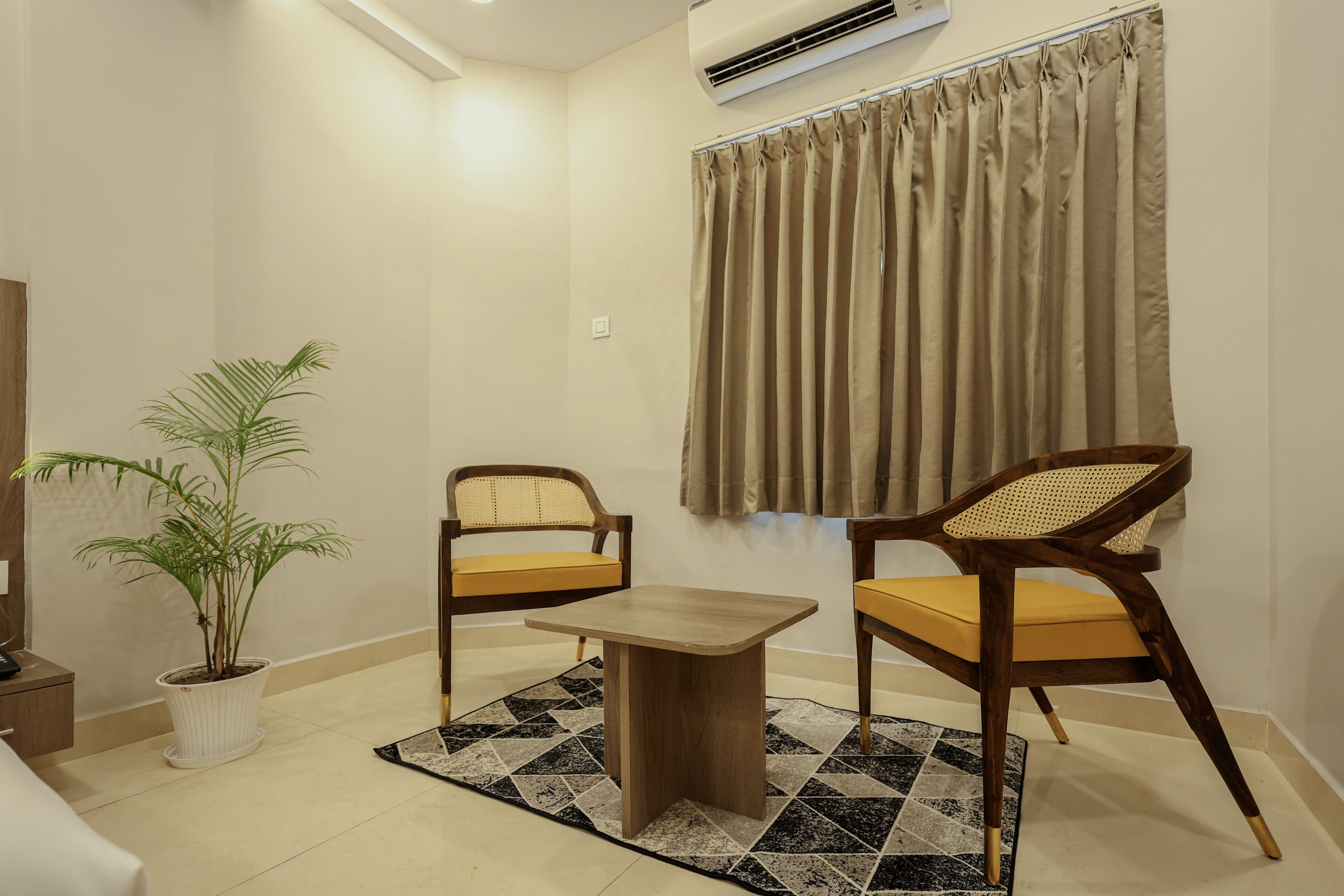 A small room with two wooden chairs, a table, a potted plant, and a window with curtains.