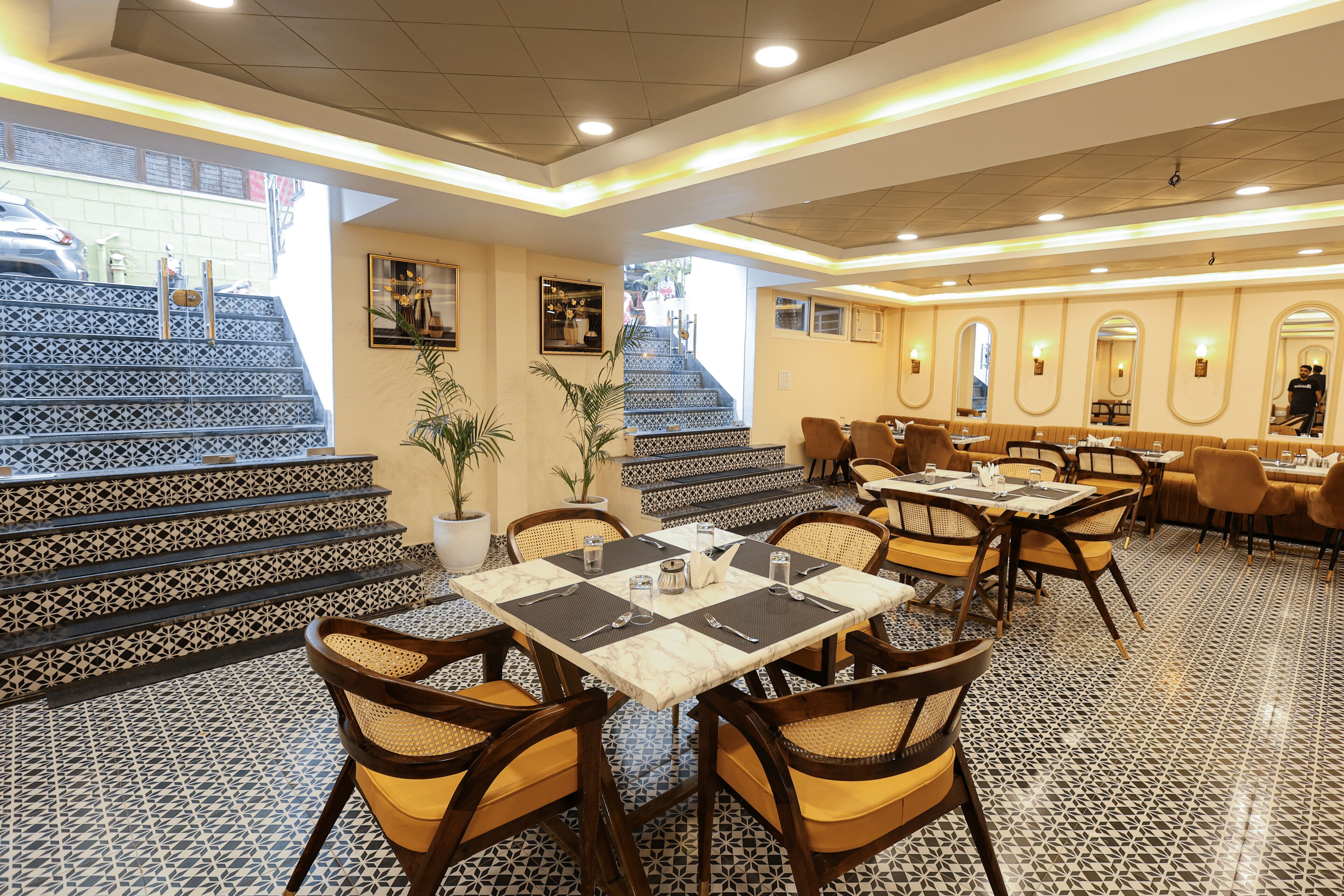 A restaurant with patterned floor tiles, multiple dining tables with chairs, and a staircase with decorative tiles leading to an outdoor area.