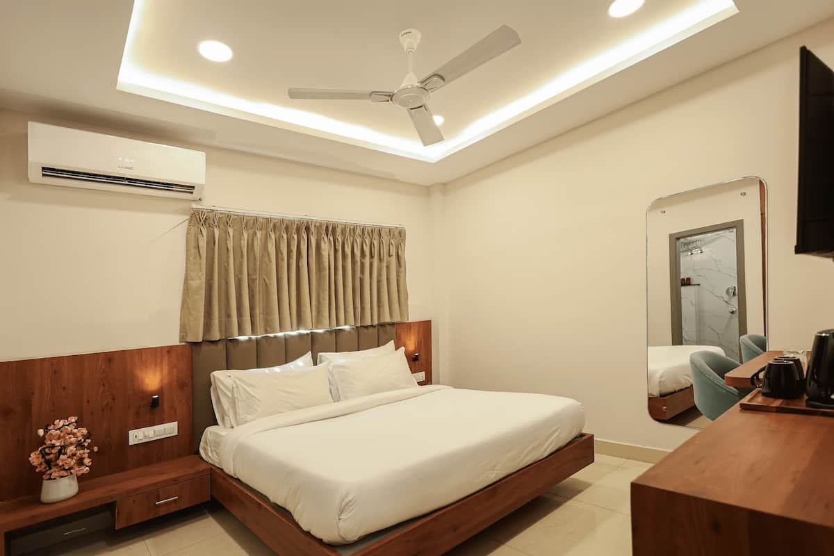 Une chambre d’hôtel moderne avec un lit en bois, un ventilateur de plafond, un appareil de climatisation, une table de chevet ornée d’un vase de fleurs et un miroir au mur.