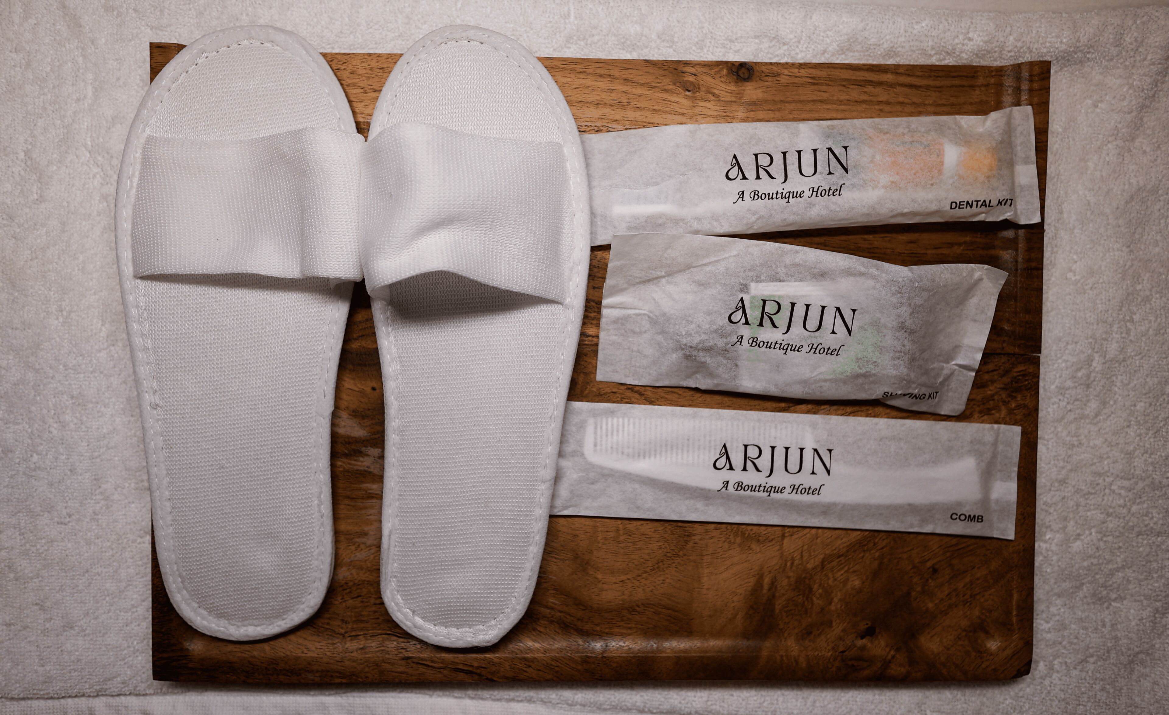 A pair of white slippers and three white packages labeled 'ARJUN A Boutique Hotel' on a wooden surface.