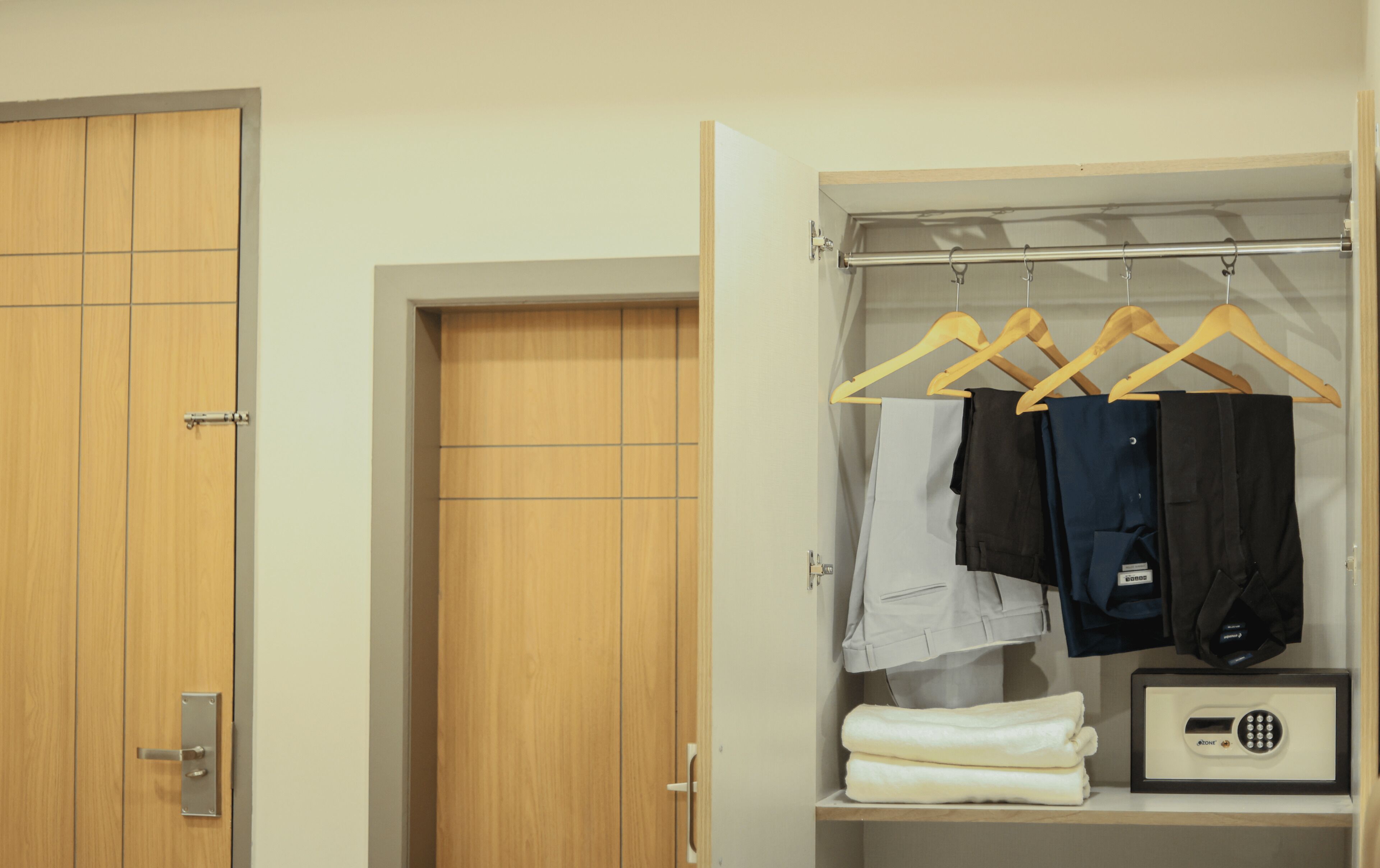 A hotel room with a wooden wardrobe, a hanging wardrobe with clothes and a safe.
