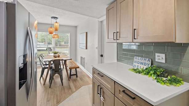 A modern kitchen with wooden cabinets, a stainless steel refrigerator, a dining area with a table and chairs, and a sign on the counter. - Del Boca Vista|Pool, Screened Porch, 5 to Beach (Largo)