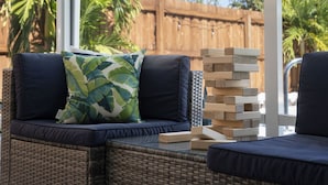 A wicker sofa with a cushion and a pillow, a stack of wooden blocks, and a wooden fence in the background. - Del Boca Vista|Pool, Screened Porch, 5 to Beach (Largo)