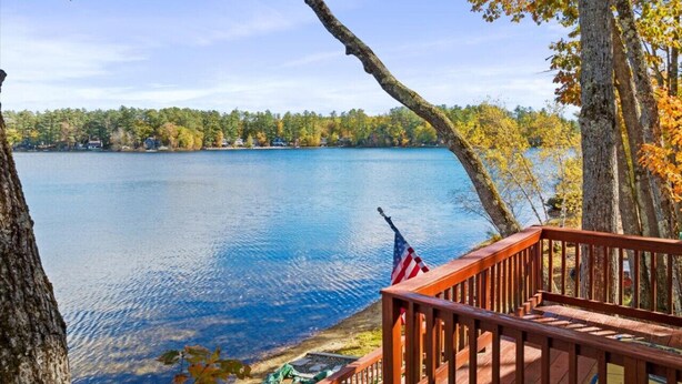 Blick auf einen See von einer Holzdielen-Terrasse mit einer US-amerikanischen Flagge, umgeben von Bäumen und blauem Himmel.
