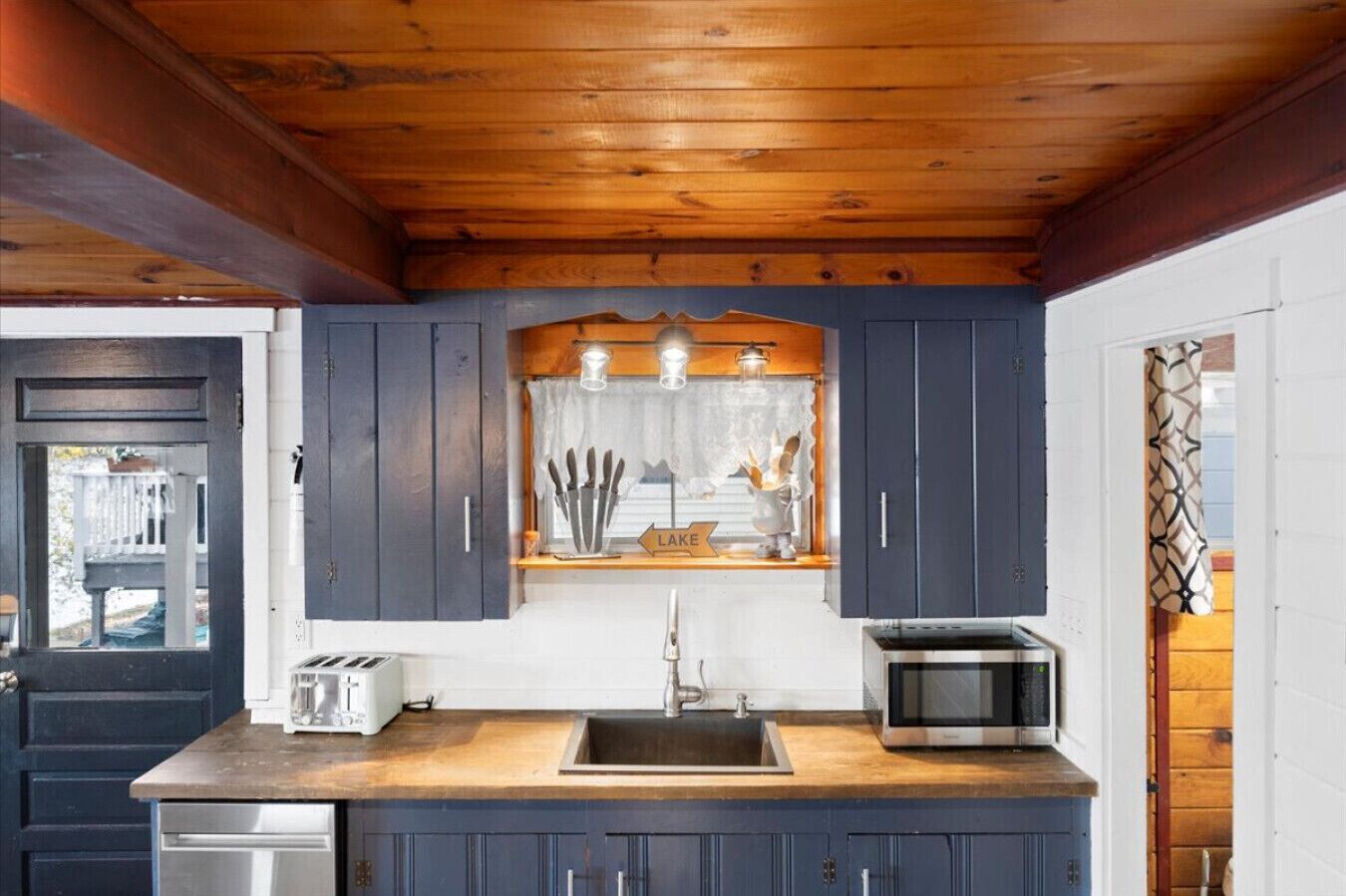 Een keuken met donkerblauwe kastjes, een houten aanrecht, een spoelbak, een broodrooster en een magnetron.