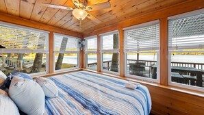 Ein Blockhauszimmer mit Bett, großen Fenstern, Deckenventilator und Blick auf einen Steg.