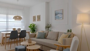 A modern living room with a sofa, chairs, a dining table, and a floor lamp. - Sunstay Cosy Flat I Cristo Malaga (Málaga)