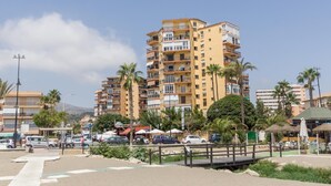 Un immeuble résidentiel à plusieurs étages, doté de balcons, d’un espace de stationnement et de palmiers.