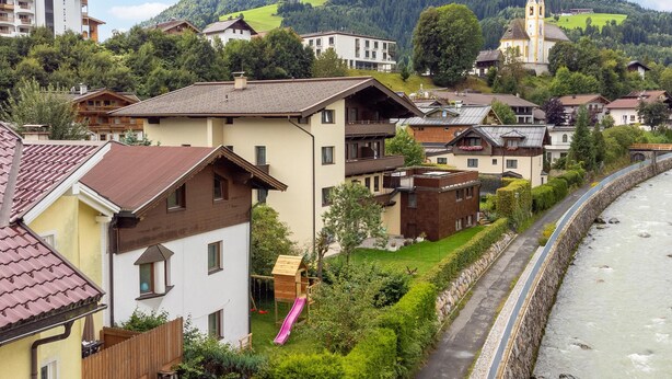 A riverside hotel with a view of a mountain and a church. - Cosy apartment in the center with a garden (Kirchberg in Tirol)