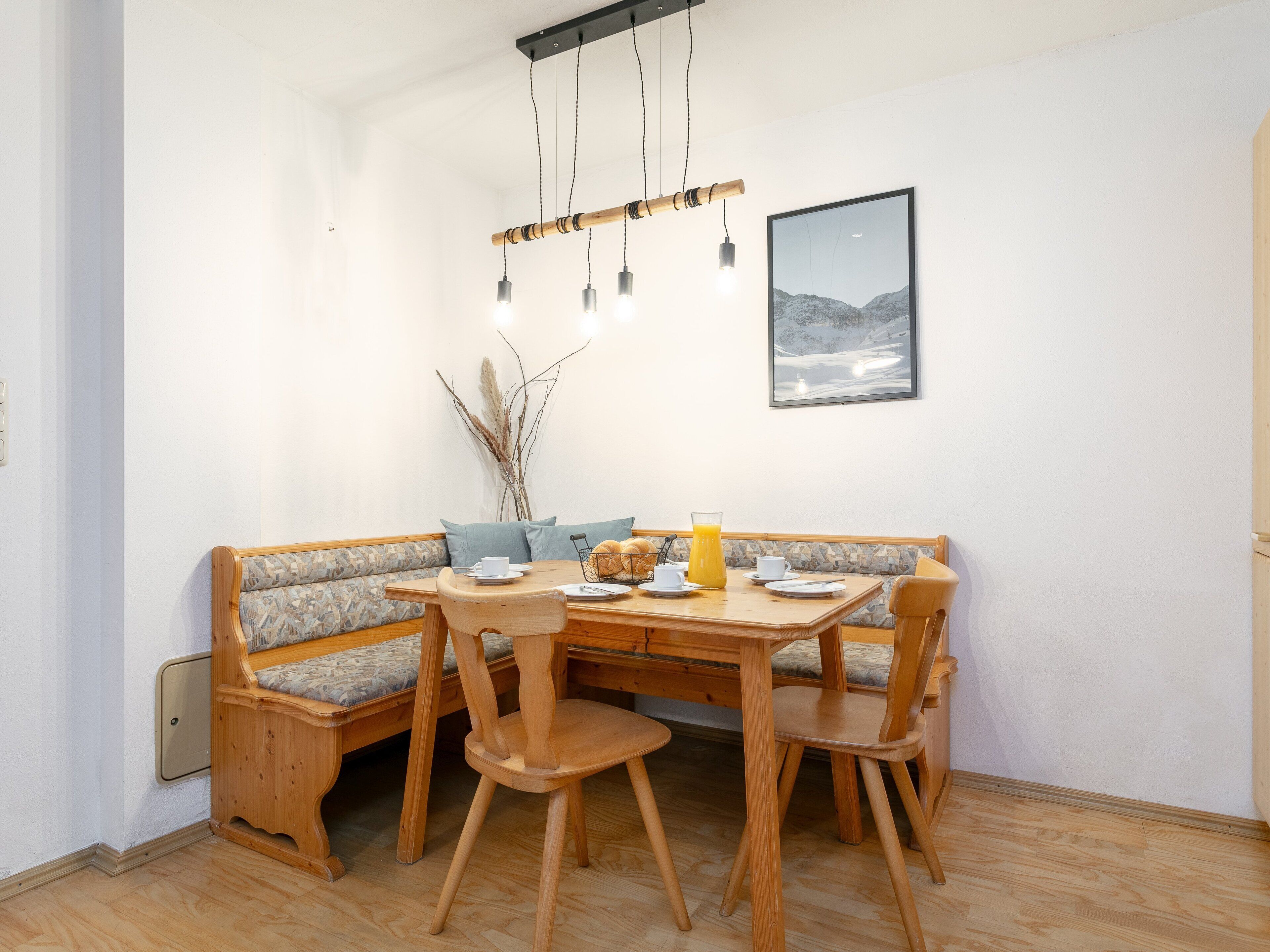 Et spiseområde med et træbord og stole, en bænk med hynder og en hængende lampe.