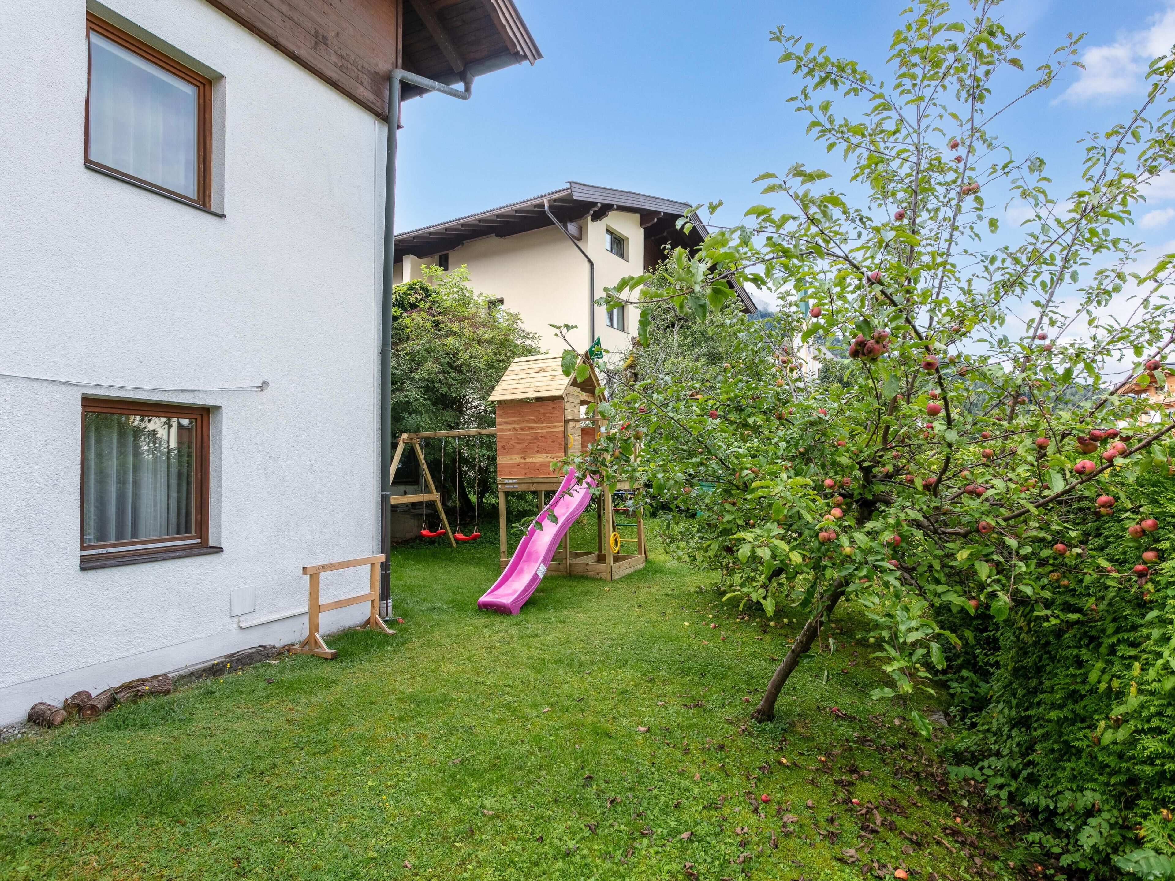 A house with a small garden, a wooden playhouse, and a slide.