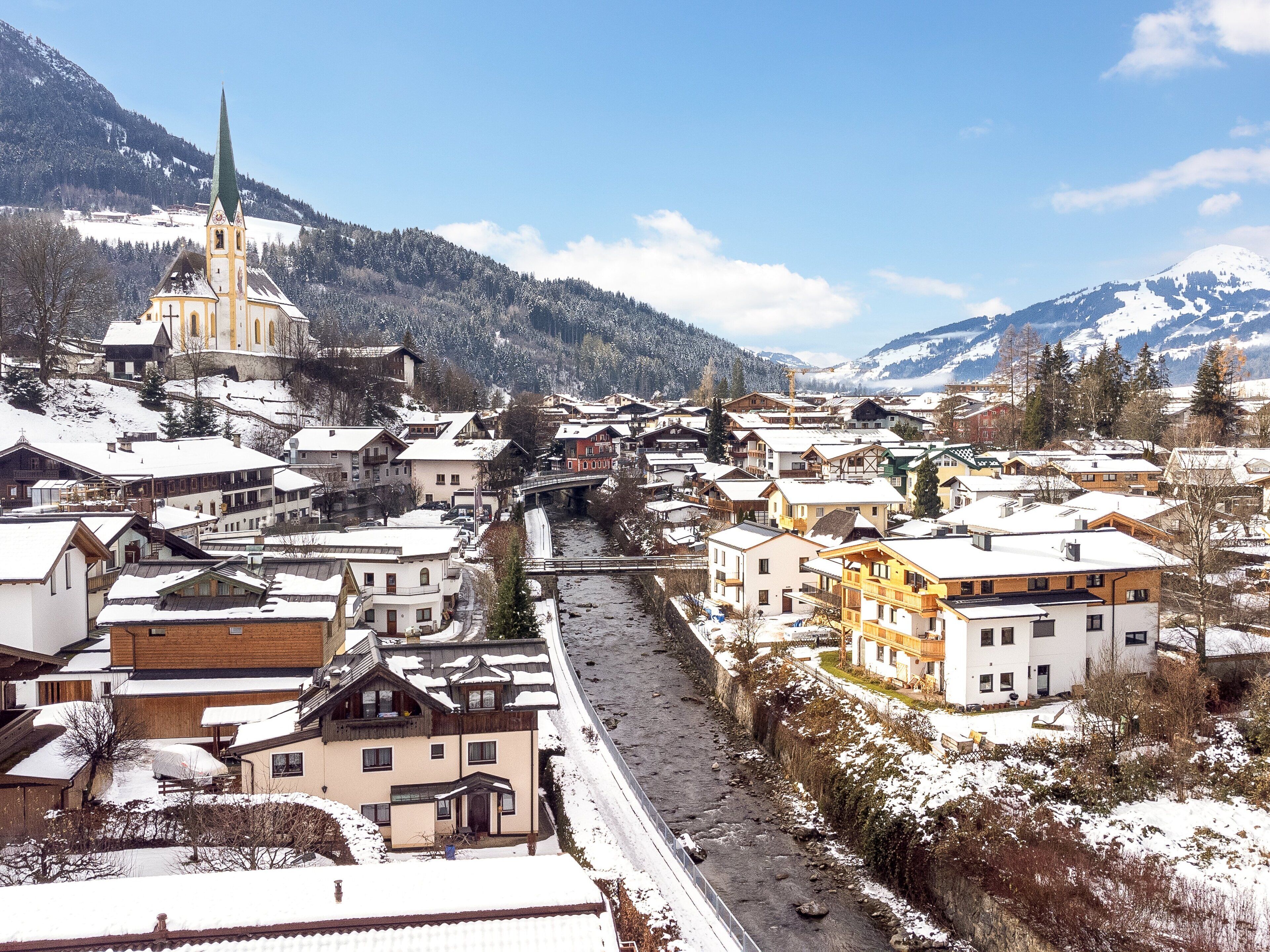 A snow-covered town with a prominent church, a river running through the center, and mountainous terrain in the background.